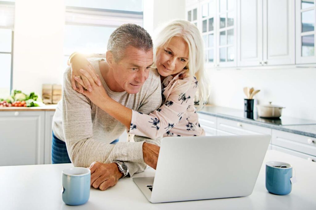 Older man and woman looking at information on their laptop in the kitchen.