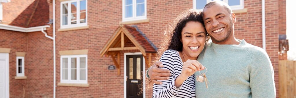 Young couple standing in front of their new home with their keys.