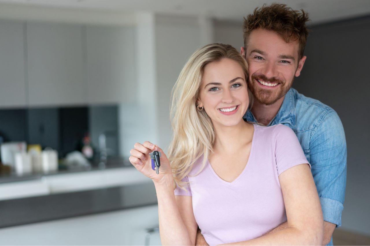 Young couple smiling while holding the keys to their new home.
