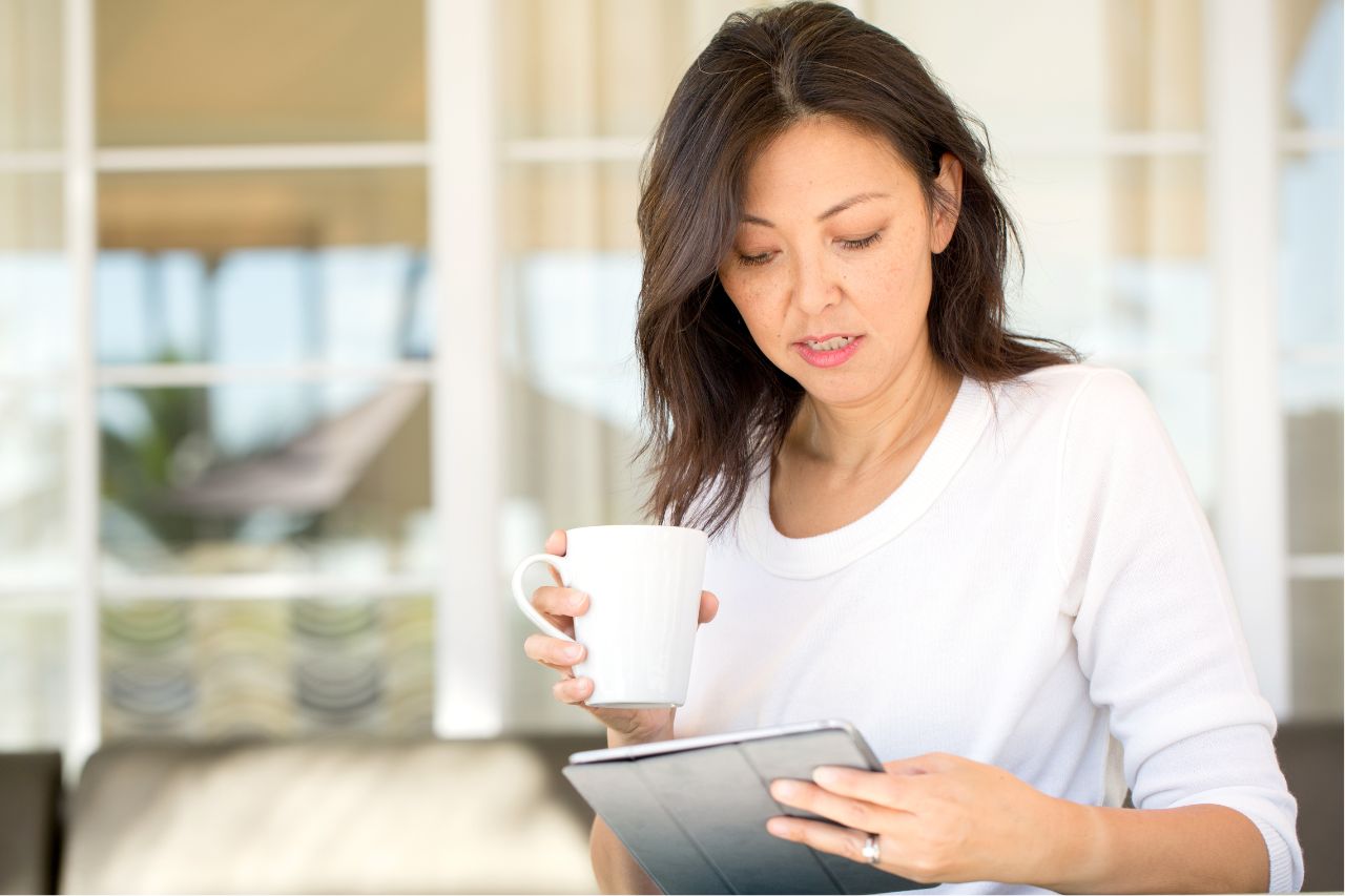 Woman looking an an iPad while drinking coffee. Woman looking an an iPad while drinking coffee.